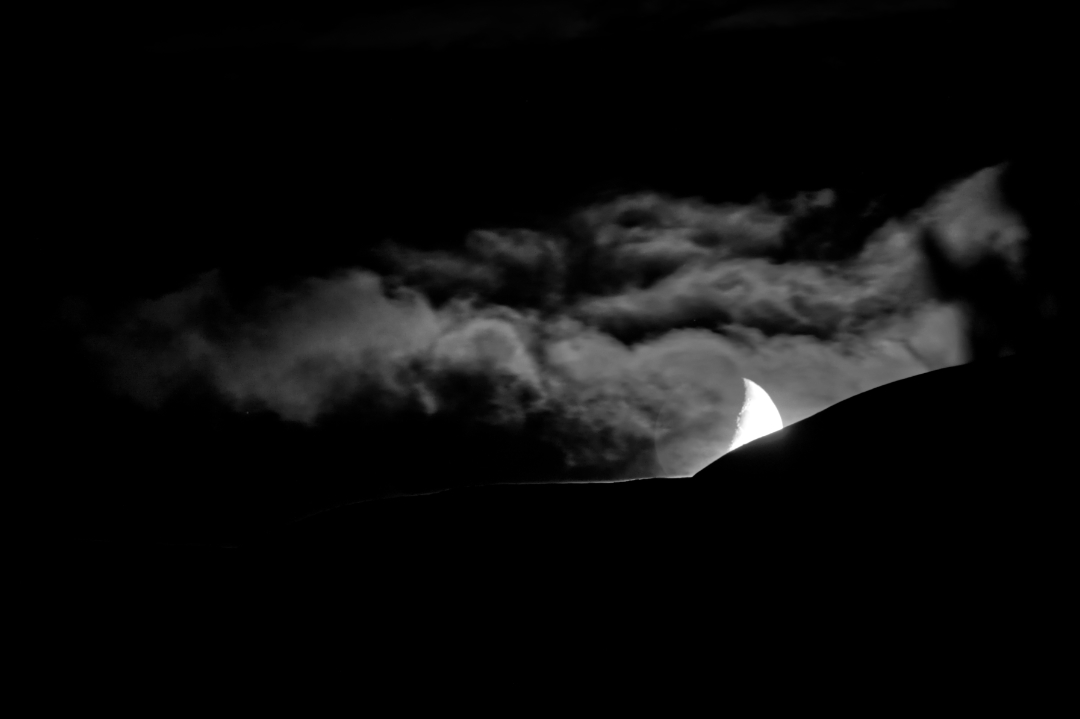 Moon setting behind a mountain, partially hidden by a cloud.